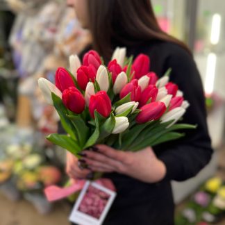 Мікс тюльпанів – букет із 29 рожевих і білих тюльпанів, перев’язаний рожевою стрічкою, тримається рукою в квітковому магазині